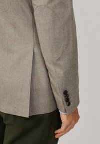 Ljusgrå blazer med texturerad väv, armbågsbricka och fyra svarta knappar vid manschetten. Har en bakventil och en något figursydd design.