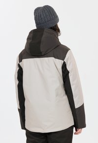 Vue arrière d'une veste bicolore, présentant un corps gris clair avec des accents gris foncé et une capuche, accompagnée d'un bonnet en tricot gris texturé.