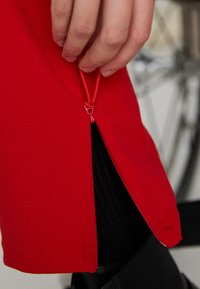 Red garment with a side zipper featuring a pull tab. The fabric appears smooth, and a black texture is visible inside the zipper opening.