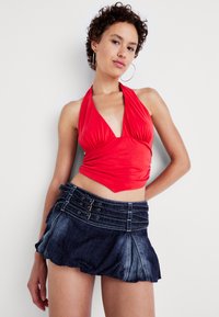 Top roșu cu sfoară, din material gathered, cu un decolteu adânc în formă de V, asortat cu o fustă mini din denim închis, care prezintă mai multe accente cu nasturi și un tiv volărit.
