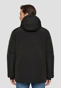 Sort polstret jakke med hætte, der har en glat tekstur og en afslappet pasform. Ingen synlige mønstre eller hardware-detaljer.