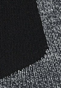 Tessuto a maglia che mostra un mix di fili neri e argento metallico. La texture è liscia con una trama stretta, caratterizzata da un contrasto di colori distintivo.