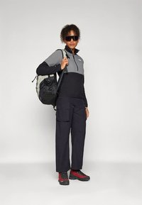 Fekete és szürke cipzáras pulóver, fekete cargo nadrág, piros-fekete túrabakancsok, valamint többrekeszes kialakítású fekete hátizsák.