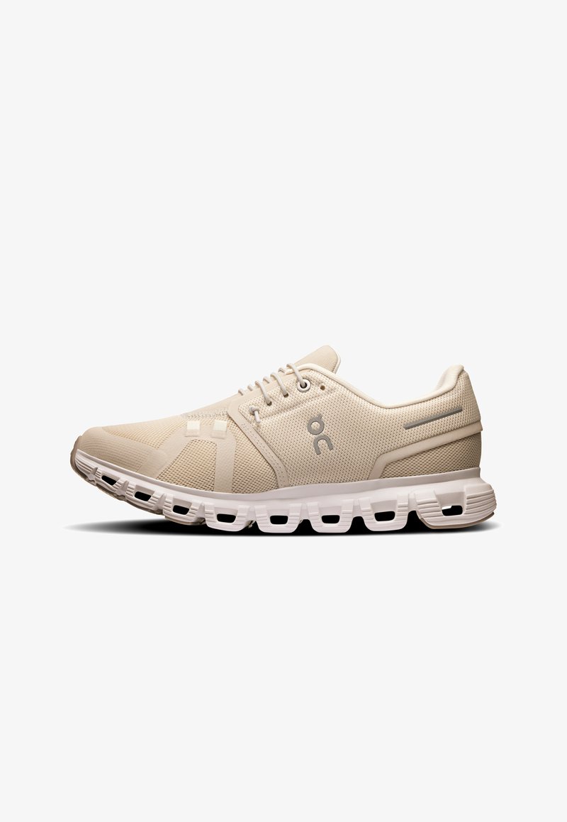Chaussure de course beige dotée d'un dessus en maille, d'accents texturés, d'une semelle arrondie et d'un rembourrage important avec des découpes pour plus de flexibilité.