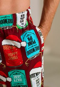 Red and turquoise pajama pants featuring a festive print of beer cans and Santa hats, with a soft, lightweight fabric and elastic waistband.