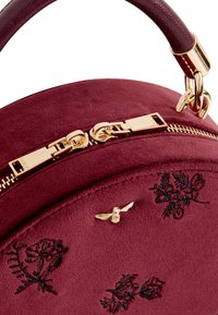 Ronde bordeaux suede tas met gouden hardware, bovenhandvat, geborduurde bloemenaccenten en een decoratieve bijmotief nabij de rits.