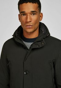 Zwarte hoodie met knoopsluiting, ritszakken en een textuur aan de binnenkant. Heeft een hoge kraag en contrasterende voering.