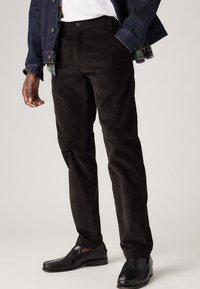 Pantalones de pana negros con un corte recto, tejido texturado y cintura de altura media, combinados con unos mocasines negros brillantes.