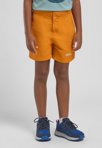 Orange Shorts mit einer glatten Textur und einem Logo auf der linken Vorderseite. Kombiniert mit blauen Sportschuhen mit grauen Akzenten.