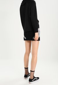 Černá mikina s kapucí, krátká džínová sukně s květinovou výšivkou, síťované ponožky a černé tenisky s bílými akcenty. Postava je zobrazena zepředu.