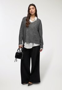 Przesadny szary sweter z błyszczącymi detalami, nałożony na biały T-shirt. Do zestawu dopasowane czarne spodnie o szerokich nogawkach oraz mała czarna torebka.