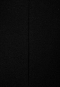 Tessuto nero con una texture a coste, caratterizzato da una cucitura centrale che corre in verticale. Il materiale appare morbido ed elastico.