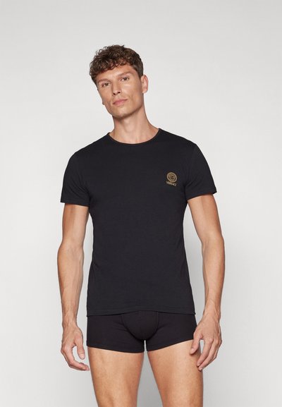 Camiseta de algodón negra con mangas cortas, cuello redondo y un logo bordado en dorado en el pecho. Diseño ajustado, textura lisa.