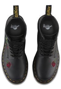Un paio di stivali neri in pelle Dr. Martens con cuciture gialle, lacci neri e fragole ricamate rosse nell'area delle punte.