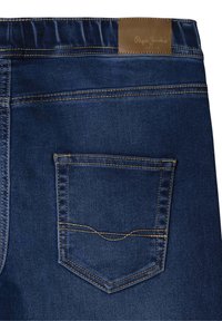 Pantalones vaqueros de mezclilla azul oscuro con bolsillo trasero, costuras en color marrón claro y etiqueta de marca de cuero marrón en la cinturilla.