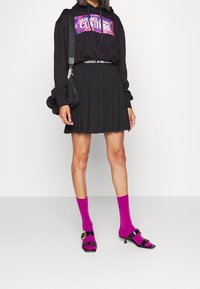 Černá mikina s kapucí a grafickým potiskem, skládánová černá minisukně, růžové podkolenky a černé sandály s přezkami.