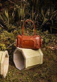 Brown leather handbag with dual handles, zip closures, and multiple pockets. Textured surface with gold-tone hardware accents.