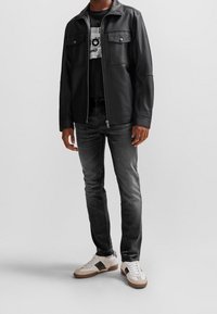 Chaqueta de cuero negra con dos bolsillos en el pecho, camiseta gris, jeans negros desgastados y zapatillas blancas con acentos marrones. Textura suave, diseño casual.