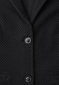Svart texturerad kavaj med ett vävt mönster, enkel knappstängning och subtila silvertrådsdetaljer för extra elegans.