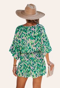 Kleurige, kortarmige romper met een groen en roze abstract patroon; lichte stof, ingezette taille en losse pasvorm. Gedragen met een strohoed.