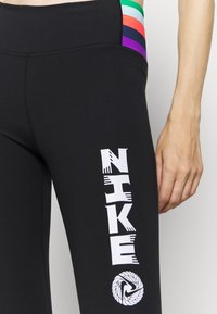 Leggings negros con cintura alta, que presentan un estampado del logo de Nike en blanco y un acento de rayas coloridas en la parte superior. Textura suave.
