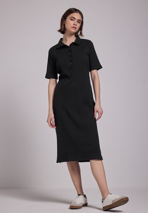 Schwarzes Rippstrickkleid mit Kragen, kurzen Ärmeln, Knopfleiste und lockerer Passform, kombiniert mit weißen Sneakers und einer Gummisohle.