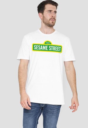 White cotton T-shirt featuring a green and yellow "SESAME STREET" graphic with the number "123" in a rounded sign shape.