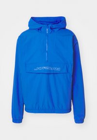 Kék szélvédő dzseki kapucnival, félig cipzáras elülső résszel, rugalmas mandzsettákkal és elülső zsebbel, amelyen fehér "JORDAN" felirat található. Könnyű anyag.