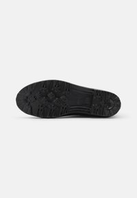 Semelle de chaussure en caoutchouc noir présentant une surface texturée avec des crampons multidirectionnels et un logo gravé, conçue pour la traction et la durabilité.