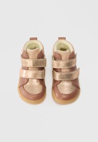 Viltinukai mažyliams su minkštu kreminiu pamušalu ir metalinėmis rožinės aukso juostomis ant šviesiai rudos odos padų, matomi iš viršaus prieš baltą foną.