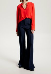Blusa rossa a maniche lunghe con scollatura a V abbinata a pantaloni a gamba larga blu navy a vita alta. Tessuto morbido e vestibilità su misura in tutto.