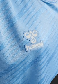 Tejido azul texturizado con un patrón de rayas claras y oscuras. Un logo azul de una abeja y la palabra "hummel" son visibles.