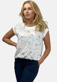 Biała bluzka z krótkim rękawem w czarne faliste wzory, z okrągłym dekoltem i marszczonym dołem; zestawiona z granatowymi spodniami.