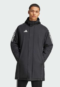 Schwarze isolierte Jacke mit einem Reißverschluss vorne, Kapuze und weißen Streifenakzenten an den Ärmeln. Mit einem Adidas-Logo auf der Brust.