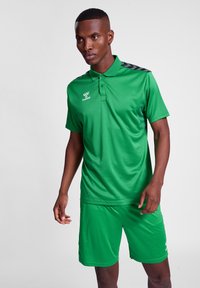 Grøn atletisk polo og shorts sæt lavet af glat stof. Poloen har en krave, sorte detaljer på skuldrene, og logoet på brystet.