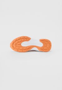 Footwear sole view; white base with textured orange outsole; features flexible grooves and rounded tabs for traction.