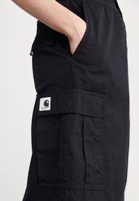 Black cargo pants featuring a side pocket, elastic waistband, and a logo patch. Material appears durable with a smooth texture.