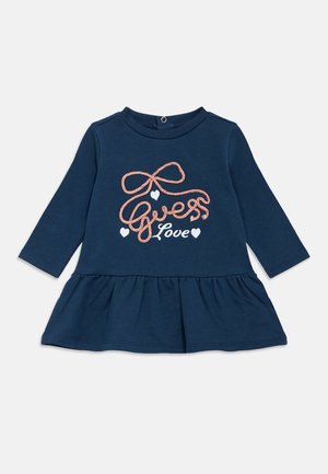 Marineblå kjole med langermet og flagrende nederkant, med rosa brodert tekst som sier "Guess Love" og små hjerter. Mykt bomullsmateriale.