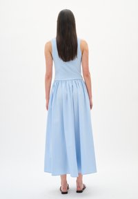 Robe bleu clair avec un haut ajusté à côtes et une jupe fluide et froncée. Texture lisse avec un ourlet large, stylée avec des sandales plates.