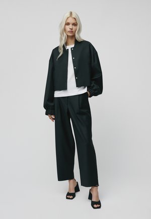 Svart cropped jakke med trykknapper, kombinert med en hvit T-skjorte og vide svarte bukser. Modellen har på seg svarte åpne hæler.