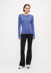 Elastična rebrasta long-sleeve majica u plavoj boji, uparena s crnim čupavim hlačama i bijelim tenisicama. Glatka tekstura i okrugli dekolte.