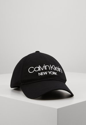 Sort baseballcap med hvidt broderet "Calvin Klein NEW YORK" logo foran, vist på en hvid overflade.