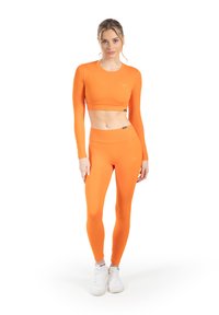 Oranje crop top met lange mouwen en hooggetailleerde legging, gemaakt van rekbare, gladde stof. Voorzien van een klein logo op de top en de tailleband.