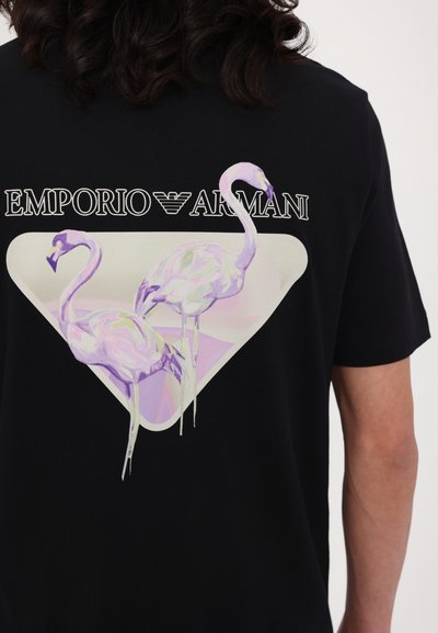 Black t-shirt featuring a large, stylized graphic of two pink flamingos within a geometric white and pastel triangle. Brand logo displayed above.