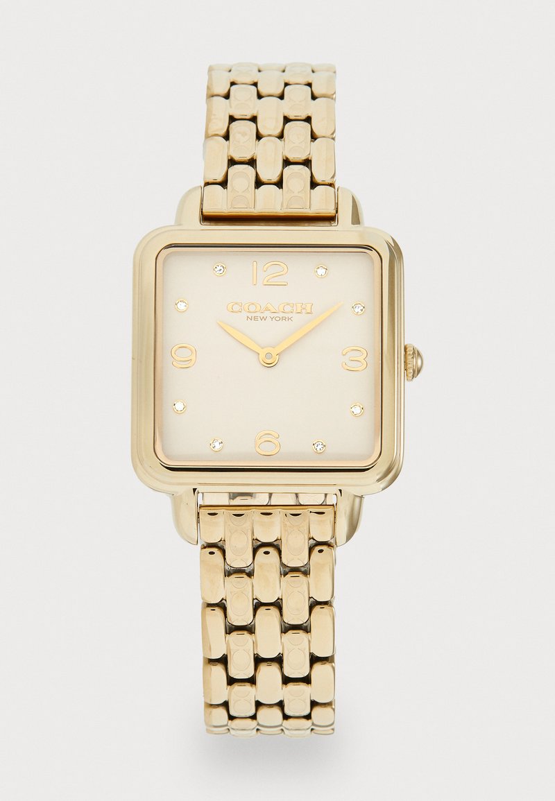 Gold rectangular watch with a textured link bracelet, featuring a cream dial, gold accents, and studded hour markers. Coach branding displayed.