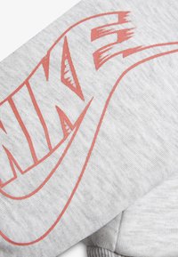 Hellgrauer Sweatshirtstoff mit strukturiertem Finish, versehen mit einem großen roten Nike-Logo und kontrastierenden Linien in einem dynamischen Stil.
