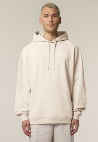 Beige, oversized kapucnis pulóver elülső zsebbel, húzózsinórral ellátott kapucnival és rugalmas mandzsettával. Puha anyagból készült, sima tapintással.