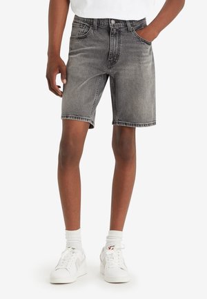 Shorts de denim en negro deslavado con un diseño clásico de cinco bolsillos, corte recto y detalles de costura visibles, combinados con zapatillas blancas.