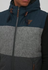 Kapuzenshirt mit einem Farbblockdesign in Dunkelblau, Grau und Schwarz. Hergestellt aus strukturiertem Stoff mit verstellbaren Kordelzügen.