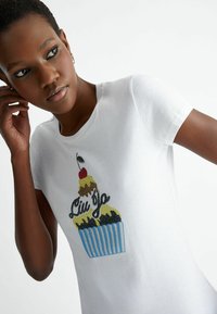 Camiseta de algodón blanca con un gráfico de cupcake con glaseado de color, una cereza y el texto "Liu Jo"; mangas cortas y escote redondo.